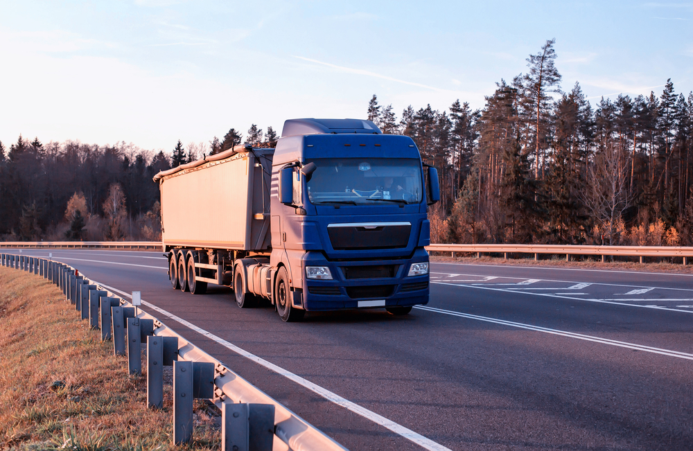 A modern truck transports bulk cargo along an asphalt road against the backdrop of a forest and sky. Concept for the transportation of solid bulk cargo in the form of grain in special trailers