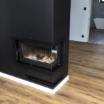 A modern fireplace with a closed combustion chamber standing in the living room, painted black, with a washed corner pane.