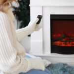 Young woman sitting near electric fireplace at home. Concept of heating season